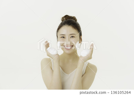 A young Japanese woman smiling with cleansing foam in both hands against a white background A young Japanese woman smiling with cleansing foam in both hands against a white background 136105264