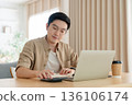 Happy young Asian man working on laptop in living room 136106174