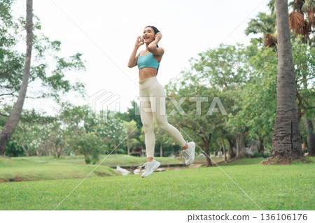 Young Asian woman in sportswear jumping happily during outdoor workout in a green park Young Asian woman in sportswear jumping happily during outdoor workout in a green park 136106176