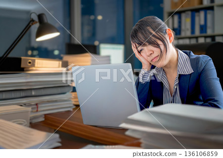 A woman who seems to be struggling with overtime work A woman who seems to be struggling with overtime work 136106859