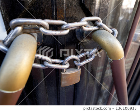 A black door securely locked with a chain and padlock 136106933