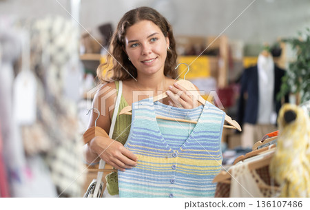 Positive young woman choosing something for summer in clothing store 136107486