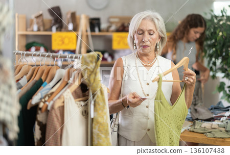 Attentive mature woman choosing something for summer in clothing store Attentive mature woman choosing something for summer in clothing store 136107488