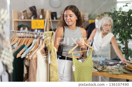 Positive young woman choosing something for summer in clothing store Positive young woman choosing something for summer in clothing store 136107490