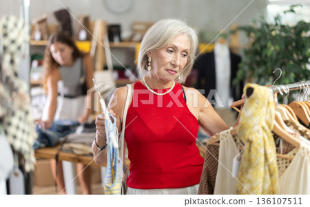 Elderly woman choosing vest in clothing store Elderly woman choosing vest in clothing store 136107511