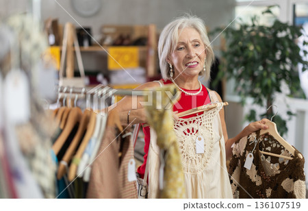 Positive mature woman choosing something for summer in clothing store 136107519