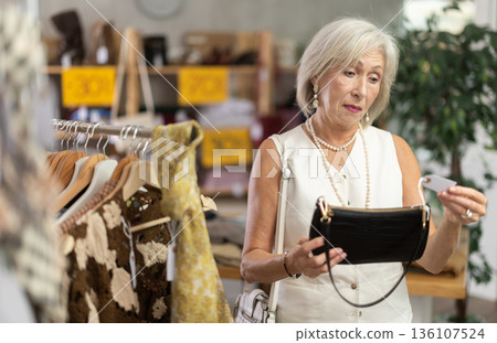 Mature woman choosing handbag in clothing store Mature woman choosing handbag in clothing store 136107524