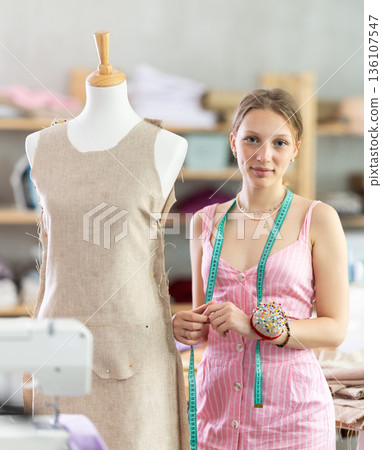 Designer in dress standing near mannequin in workshop 136107547