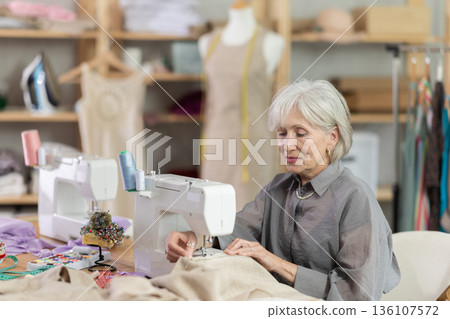 woman dressmaker sews on a machine in a workshop woman dressmaker sews on a machine in a workshop 136107572