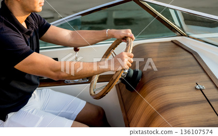 Young man on sailing yacht. Hands hold steering wheel Young man on sailing yacht. Hands hold steering wheel 136107574