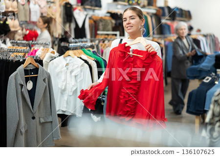 Smiling girl choosing colorful clothes in dressing room in showroom Smiling girl choosing colorful clothes in dressing room in showroom 136107625