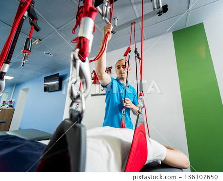 Physiotherapy. Suspension training therapy. Young man doing fitness traction Physiotherapy. Suspension training therapy. Young man doing fitness traction 136107650