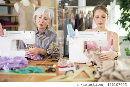 Two female dressmakers working with sewing-machine in tailor's workshop 136107655