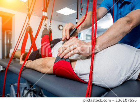 Physiotherapy. Suspension training therapy. Young man doing fitness traction Physiotherapy. Suspension training therapy. Young man doing fitness traction 136107656