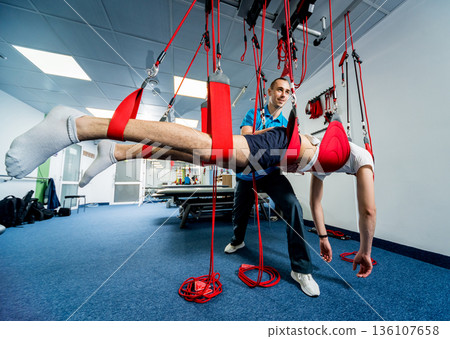 Physiotherapy. Suspension training therapy. Young man doing fitness traction Physiotherapy. Suspension training therapy. Young man doing fitness traction 136107658
