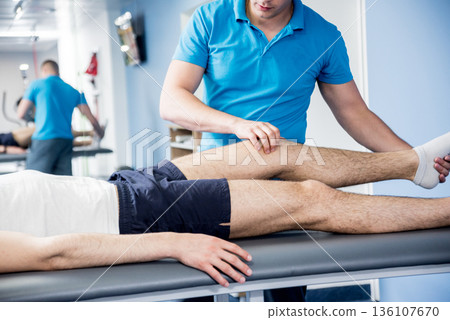 Rehabilitation therapy. Physiotherapist working with young male patient  136107670