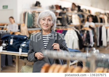 Old woman watching excitedly large stock of clothes in clothing store 136107671