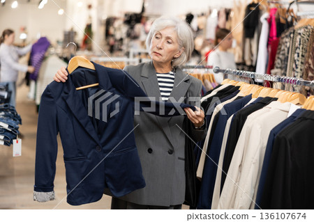 Elderly woman trying on a new jacket in clothing boutique Elderly woman trying on a new jacket in clothing boutique 136107674