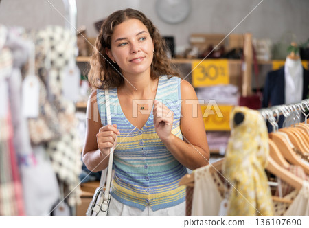 Young woman chooses a set of clothes for the summer. Visitor to the boutique examines new summer collection of clothes Young woman chooses a set of clothes for the summer. Visitor to the boutique examines new summer collection of clothes 136107690