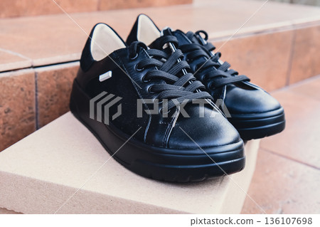 Elegant black leather womens shoes blank product for branding displayed on recycled cardboard box. New casual female sneakers no-brand footwear e-commerce. No logo product 136107698