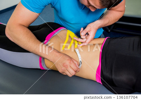 Kinesiotaping. Physical therapist applying tape to young beautiful womans spine Kinesiotaping. Physical therapist applying tape to young beautiful womans spine 136107704