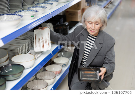 Senior woman in supermarket is choosing square plates with oriental style 136107705