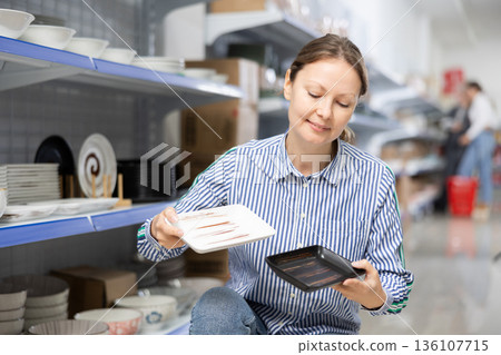 Woman in supermarket is choosing square plates 136107715