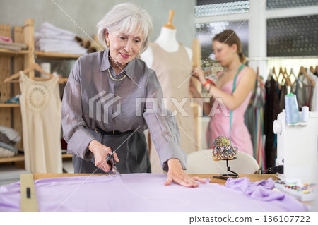 Mature female dressmaker cutting textile other work with mannequin Mature female dressmaker cutting textile other work with mannequin 136107722