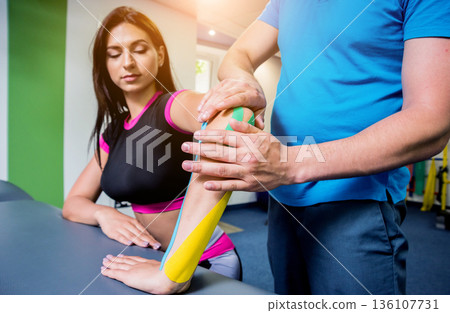 Kinesiotaping. Physical therapist applying tape to young beautiful womans spine Kinesiotaping. Physical therapist applying tape to young beautiful womans spine 136107731