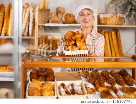 senior bakery worker sells croissants and shows off a variety of crescent-shaped buns. 136107743