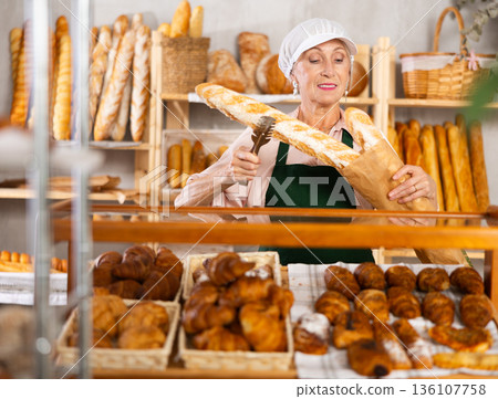 Elderly female bakery salesperson offers to buy bread, baguettes and croissants Elderly female bakery salesperson offers to buy bread, baguettes and croissants 136107758