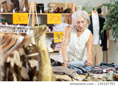 Elderly woman chooses fashionable jeans in clothing store for summer season Elderly woman chooses fashionable jeans in clothing store for summer season 136107765