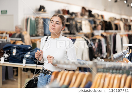 Positive joyful young woman looking for fashionable clothes in clothing boutique 136107781