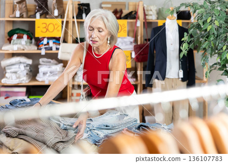 Elderly woman chooses fashionable jeans in clothing store for summer season Elderly woman chooses fashionable jeans in clothing store for summer season 136107783