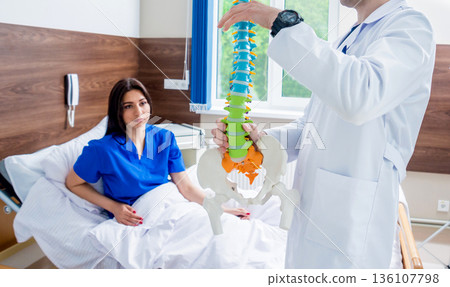 Orthopedist showing spine model to patient in hospital 136107798