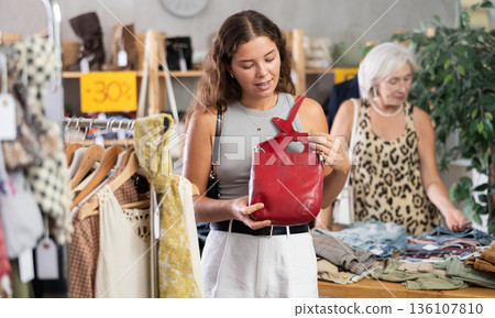 Young woman shopping - choosing a fashionable handbag in clothing store Young woman shopping - choosing a fashionable handbag in clothing store 136107810