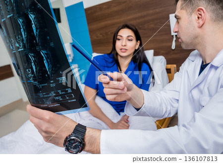 Traumatologist showing MRI film to patient in hospital. Traumatologist showing MRI film to patient in hospital. 136107813