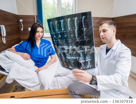 Traumatologist showing MRI film to patient in hospital. Traumatologist showing MRI film to patient in hospital. 136107819
