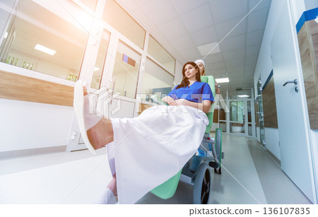 Nurse moves mobile medical chair with patient at hospital. Medical equipment. 136107835