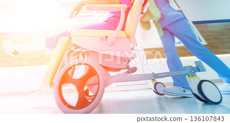 Nurse moves mobile medical chair with patient at hospital. Medical equipment. 136107843