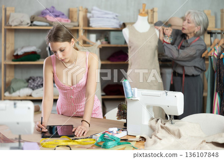 Young female dressmaker drawing in tablet other work with mannequin 136107848
