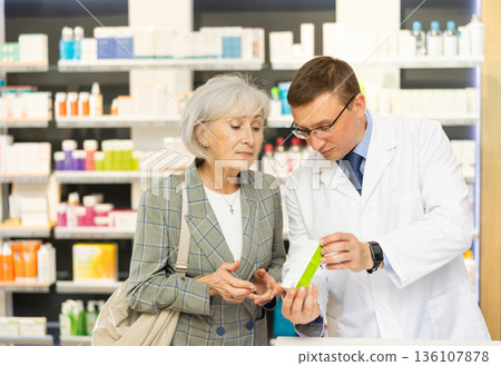 Middle-aged male pharmacist consulting old woman costumer about care product in box Middle-aged male pharmacist consulting old woman costumer about care product in box 136107878