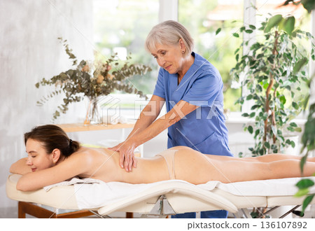 Elderly woman doing back massage to young woman 136107892