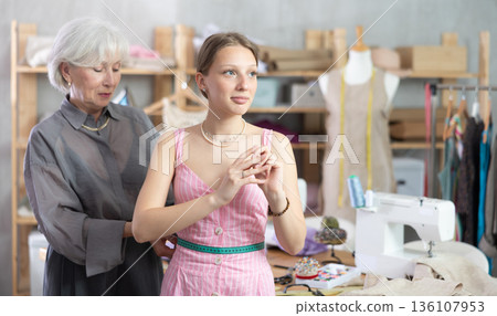 Elderly seamstress takes body measurements from young woman Elderly seamstress takes body measurements from young woman 136107953