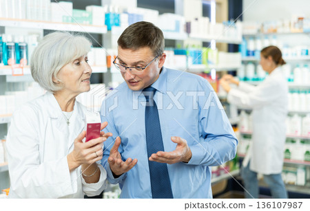 Male customer consulting with mature female pharmacist at pharmacy Male customer consulting with mature female pharmacist at pharmacy 136107987