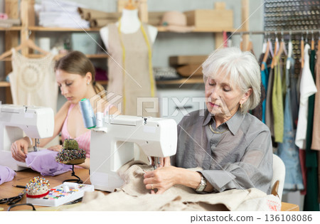 Two seamstresses sitting and working in the workshop Two seamstresses sitting and working in the workshop 136108086