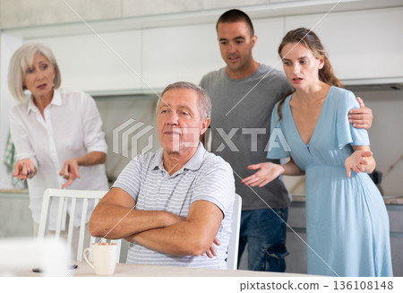 Portrait of thoughtful elderly man who had conflict with his wife and adult children while cooking dinner in kitchen Portrait of thoughtful elderly man who had conflict with his wife and adult children while cooking dinner in kitchen 136108148
