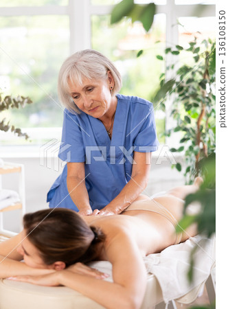 Elderly woman doing back massage to young woman 136108150