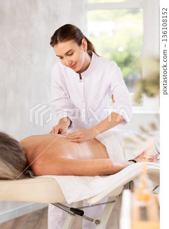 Unrecognizable elderly woman lies face down on couch and enjoy spa treatments, shoulder massage 136108152