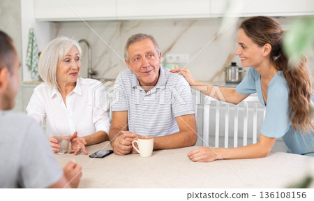 Smiling parents and adult children sit at the table with tea and talk about home life 136108156